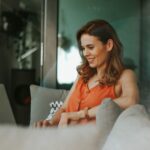 Frau im Homeoffice sitzt auf einem Sofa mit Laptop in der Hand und freut sich über Work-Life-Balance