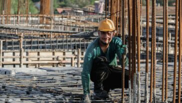 Ein Bauarbeiter kniet auf dem unvollendeten Flachdach einer Baustelle.