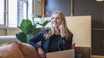 Frau telefoniert im Büro mit Laptop auf dem Schoß
