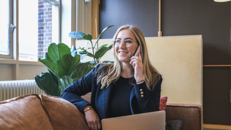 Frau telefoniert im Büro mit Laptop auf dem Schoß