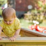 Kinderbetreuung Oberösterreich: Ein Kleines Kind versucht eigenständig aus dem Sandkasten zu steigen.