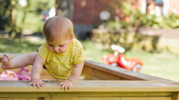 Kinderbetreuung Oberösterreich: Ein Kleines Kind versucht eigenständig aus dem Sandkasten zu steigen.