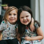 NÖ Kinderbetreuung: Zwei Kinder sitzen auf einer Stufe und grinsen.