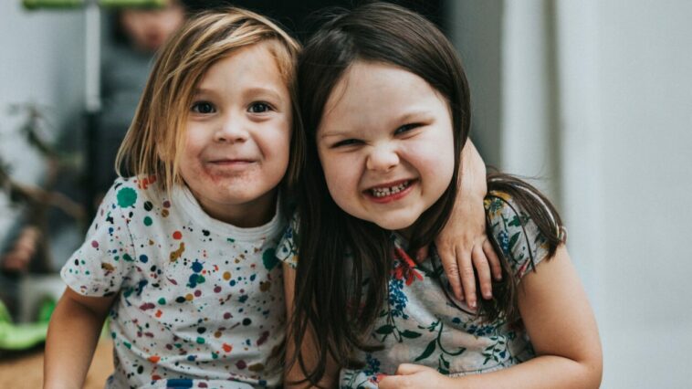 NÖ Kinderbetreuung: Zwei Kinder sitzen auf einer Stufe und grinsen.