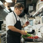 Vegane Kochlehre, am Bild ist ein Koch in einer großen Gastro-Küche mit Gemüse in der Hand zu sehen.