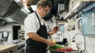 Vegane Kochlehre, am Bild ist ein Koch in einer großen Gastro-Küche mit Gemüse in der Hand zu sehen.