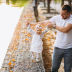 Ein Vater führt sein Kind in den Blättern spazieren. Die Kinderbetreuung ist in Oberösterreich in vielen Gemeinden mangelhaft.