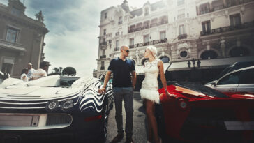 Reiche gönnen sich trotz Krise einen luxuriösen Lebensstil. Am Bild sieht man ein Pärchen zwischen zwei Luxusautos posieren.