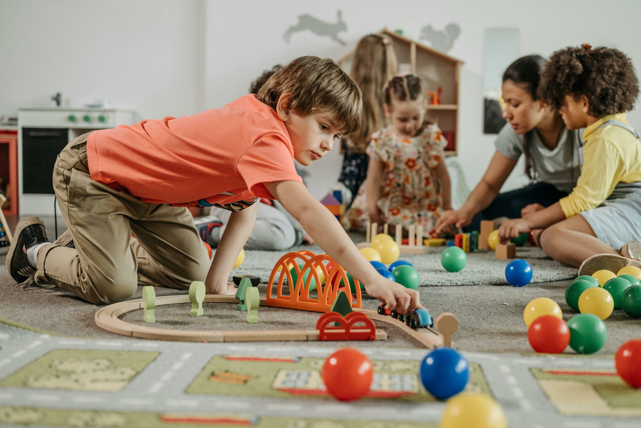 Photo by Pavel Danilyuk: https://www.pexels.com/photo/boy-in-orange-shirt-playing-train-toy-on-the-floor-8422249/ neuezeit.at Niederösterreich Kinderbetreuung