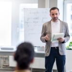 Ein Lehramt Quereinsteiger steht vor seiner Tafel und erklärt seinen Schüler:innen etwas.