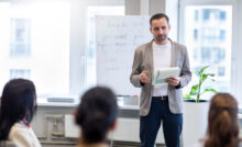 Ein Lehramt Quereinsteiger steht vor seiner Tafel und erklärt seinen Schüler:innen etwas.