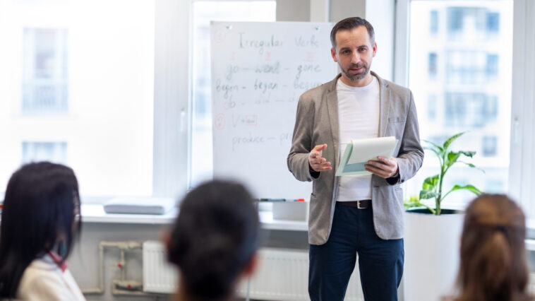 Ein Lehramt Quereinsteiger steht vor seiner Tafel und erklärt seinen Schüler:innen etwas.