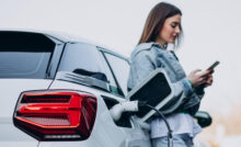 E-Auto lädt und Besitzerin steht daneben und wartet mit ihrem Handy
