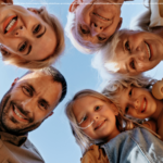 Die Armutsgefährdung im Burgenland sinkt erneut. Ob für die jüngere Generation oder die ältere - betreffen wird diese positive Entwicklung alle. Am Bild sind ein Vater, eine Mutter, zwei Großmütter und zwei Mädchen zu sehen, die im Kreis nach unten blicken, so als würden sie sich über ein Baby-Bett neigen.