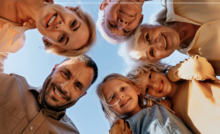 Die Armutsgefährdung im Burgenland sinkt erneut. Ob für die jüngere Generation oder die ältere - betreffen wird diese positive Entwicklung alle. Am Bild sind ein Vater, eine Mutter, zwei Großmütter und zwei Mädchen zu sehen, die im Kreis nach unten blicken, so als würden sie sich über ein Baby-Bett neigen.