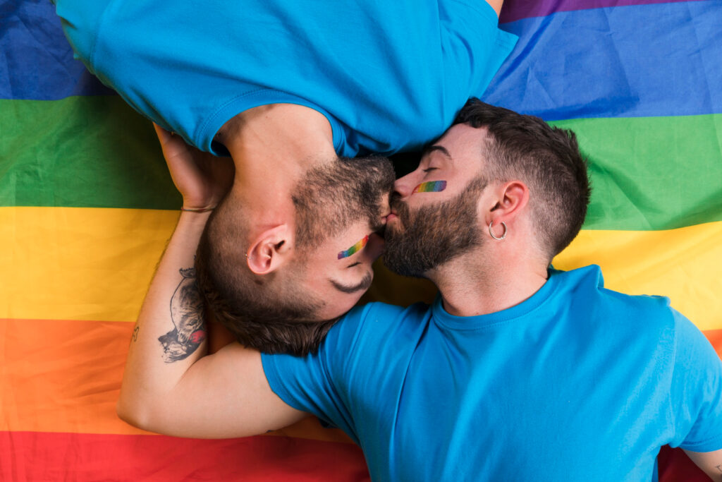 queeres Pärchen küsst sich vor einer Regenbogenflagge good-news-in-oesterreich
