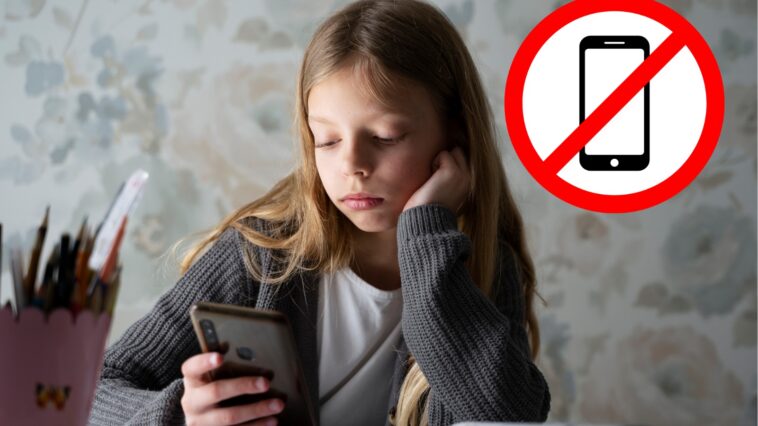 Mädchen sitzt am Handy während neben ihr Schulbücher geöffnet sind. Daneben ist ein großes "Handy verboten"-Zeichen. handyverbot-schule-oesterreich