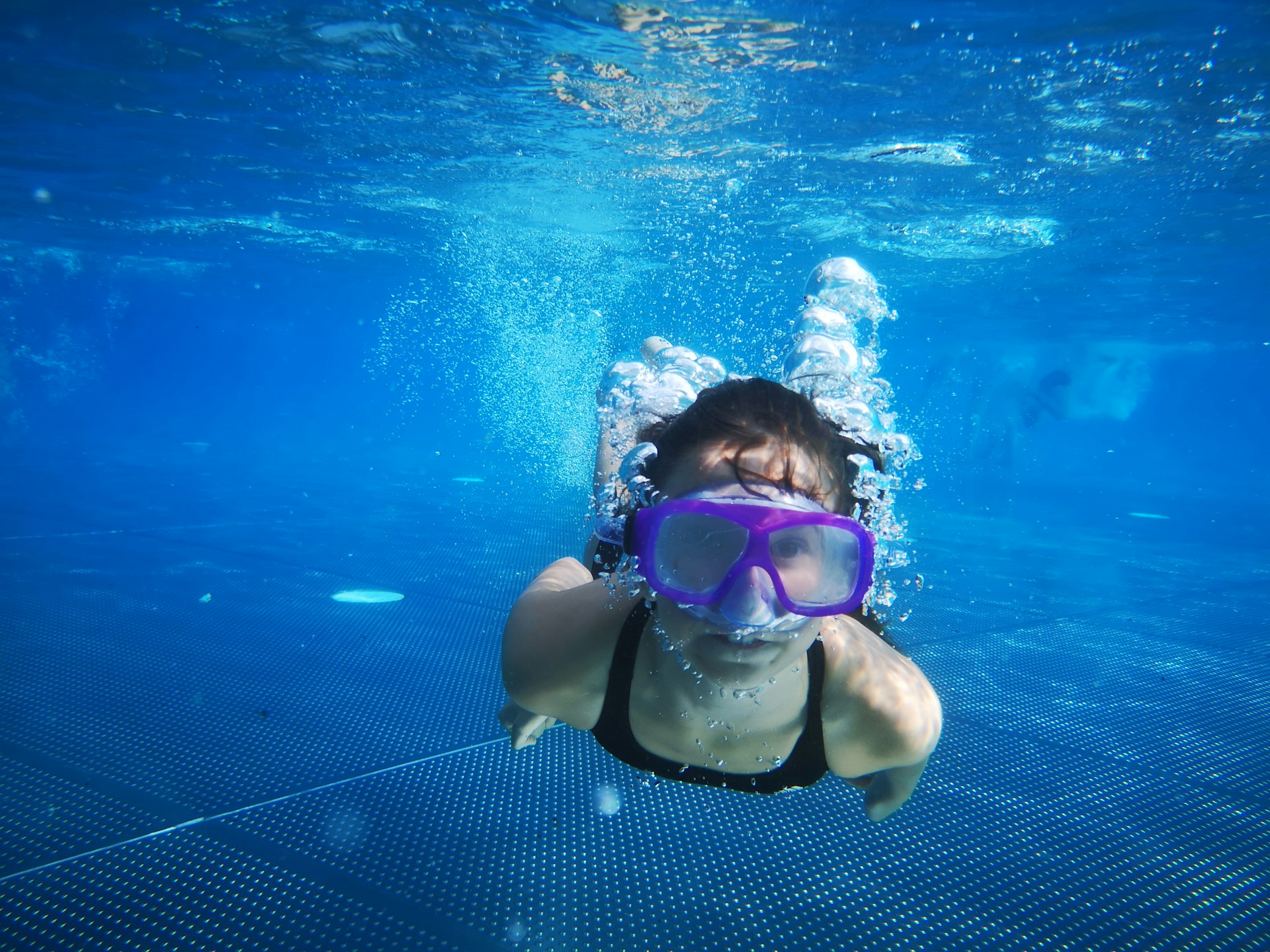 Ein Kind mit Taucherbrille unter Wasser im Freibad