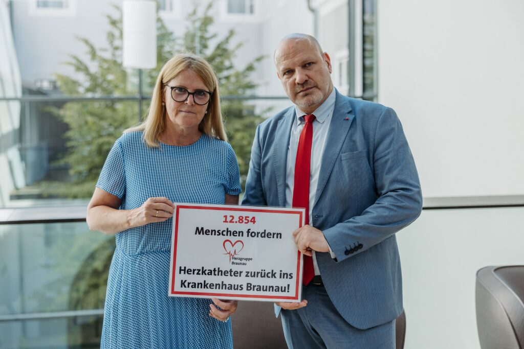 Das Foto zeigt SPÖ-Landtagsabgeordnete Gabriele Knauseder und SPÖ-Gesundheitssprecher Peter Binder mit einer Tafel, die auf die gesammelten Unterschriften für einen Herzkatheter im Krankenhaus Braunau verweist.