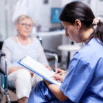 Das Foto zeigt eine Ärztin mit einer Patientin im Rollstuhl in einem Krankhaus.