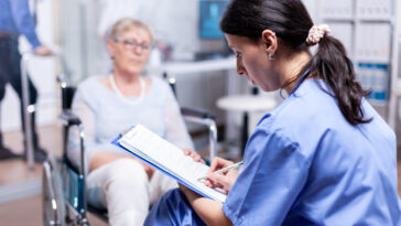 Das Foto zeigt eine Ärztin mit einer Patientin im Rollstuhl in einem Krankhaus.