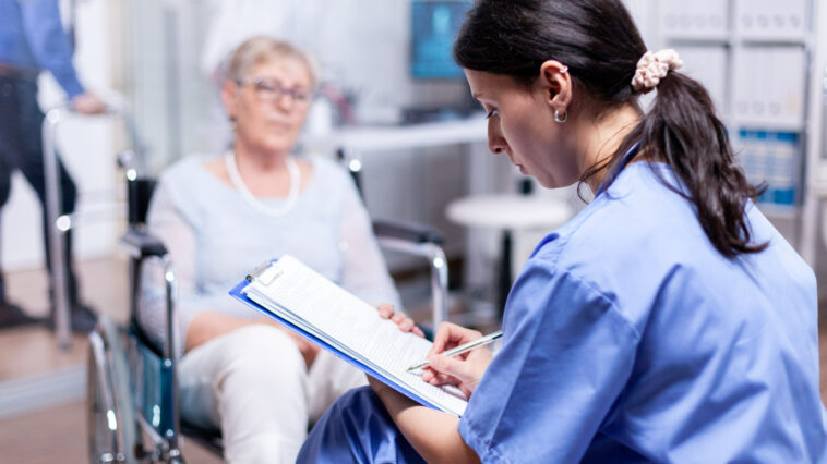 Das Foto zeigt eine Ärztin mit einer Patientin im Rollstuhl in einem Krankhaus.