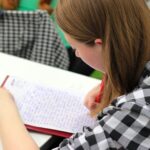 A young student writing in a notebook during a study session indoors.