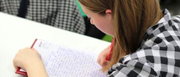A young student writing in a notebook during a study session indoors.